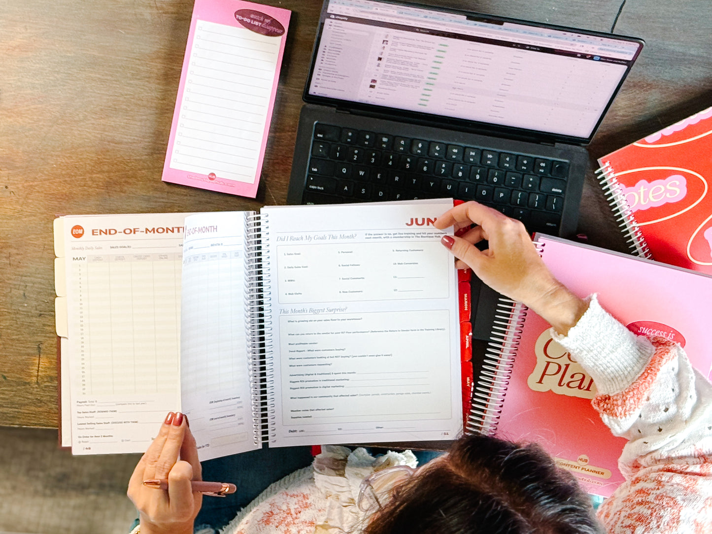Person using a planner with a laptop and notepads on a wooden table