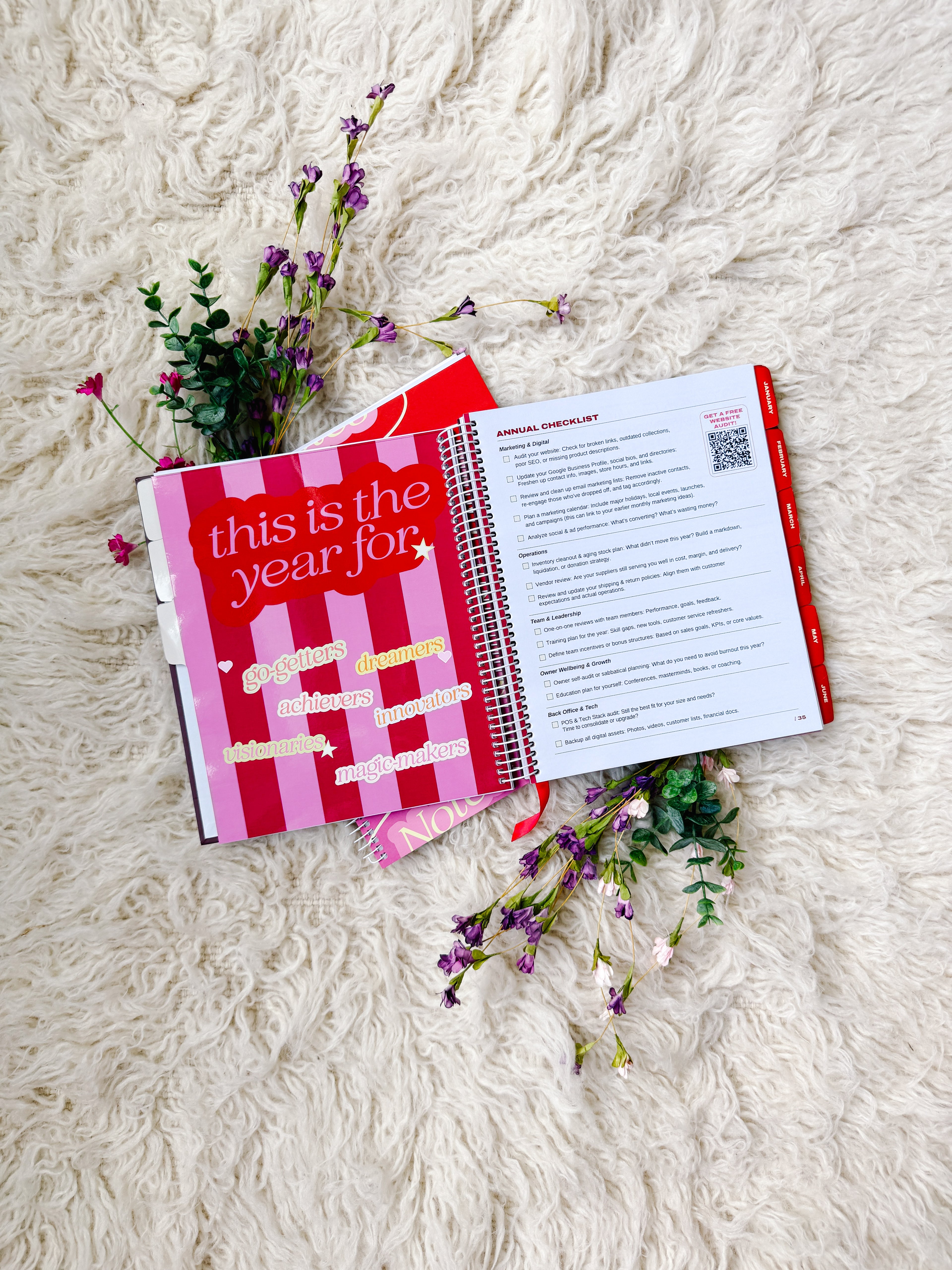 Open planner with a pink cover and red stripes on a white textured surface with flowers.