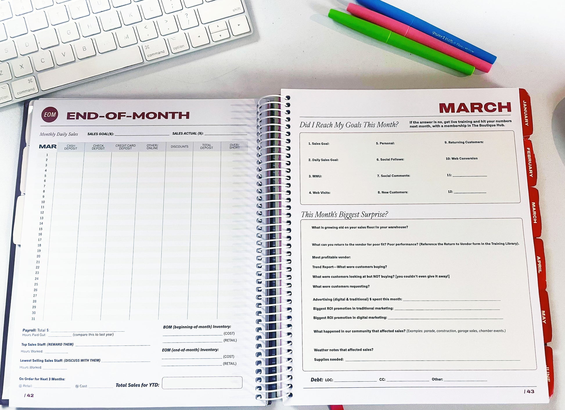 Open planner with monthly layout on a desk with a keyboard and pens.