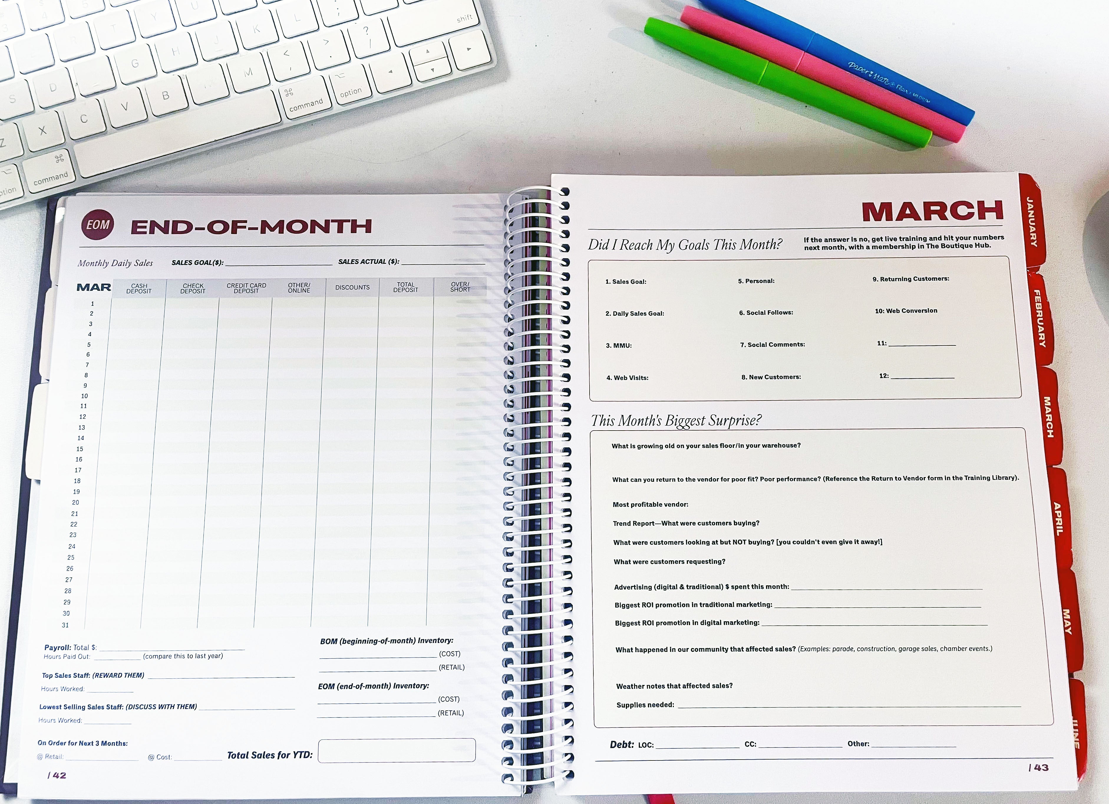 Open planner with monthly layout on a desk with a keyboard and pens.