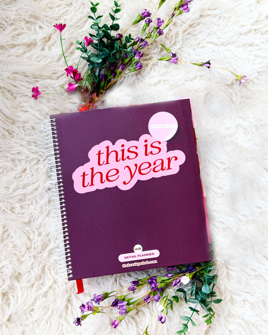 Purple planner with 'this is the year' text on a white surface with flowers